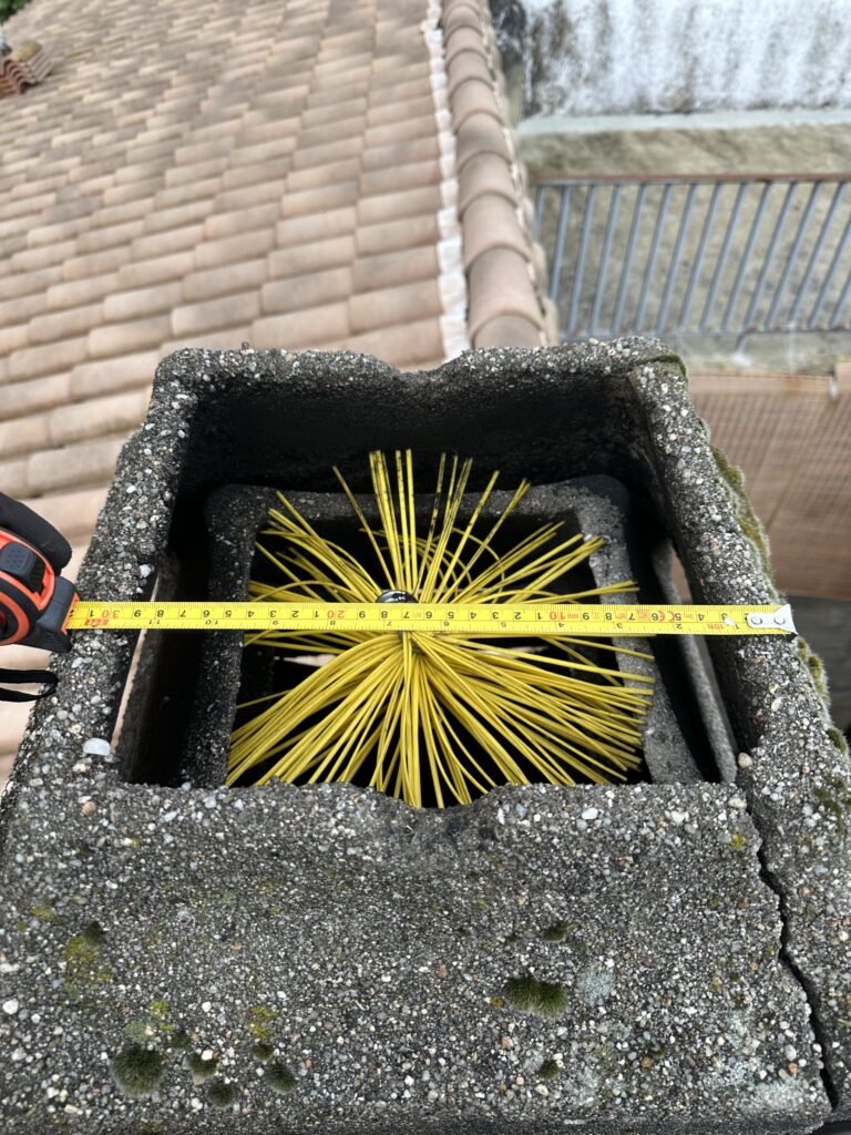 Deshollinador limpiando el cabezal de una chimenea con cepillo profesional en Navarra